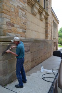 Friend of St. William John Wira attempts to clean spray paint off the walls of St. William in Price Hill after the church was defaced by vandals. (CT Photo/Megan Walsh)
