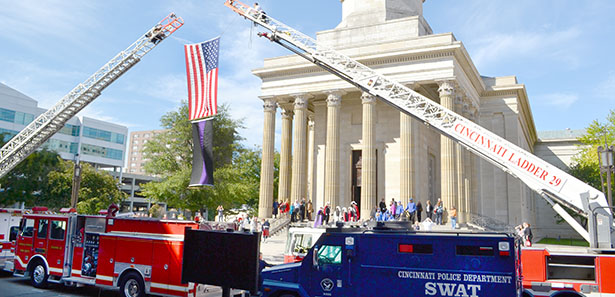An American flag and a flag of mourning hang from between two Cincinnati Fire Department ladder trucks Sept. 14 before a Blue Mass celebrated at the Cathedral of St. Peter in Chains. A Cincinnati police SWAT vehicle is also visible. These vehicles, and others, were blessed prior to the Mass. (CT Photo/John Stegeman)