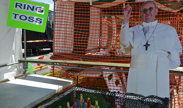 Pope Francis, or rather a cardboard cutout of him, watches over the ring toss booth as preparations continue at Holy Trinity parish in Norwood for the church's festival, which begins tonight. (CT Photo/John Stegeman)