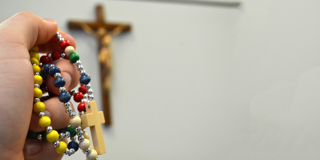 A hand holds a rainbow-colored rosary in front of a crucifix. Rainbow imagery is often associated with LGBTQ movements. Courage International, an apostolate for Catholics with homosexual desires, uses only a crucifix and the group's name as a logo. (CT Photo/John Stegeman)