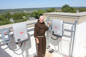 Franciscan Father Al Hirt, pastor of St. Monica-St. George Parish Newman Center, prepares to throw the switch on the inverters that convert solar power DC to alternating current on the roof of the parish center recently. (Courtesy Photo)