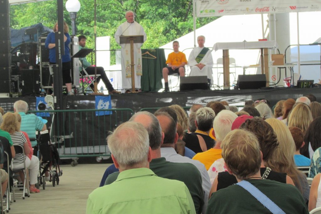 Father David Byrne celebrates Mass. Also on the stage/sanctuary: a sign language interpreter from the festival, two unidentified men who read the first two readings, and Deacon Michael Leo (CT Photo/Gail Finke)