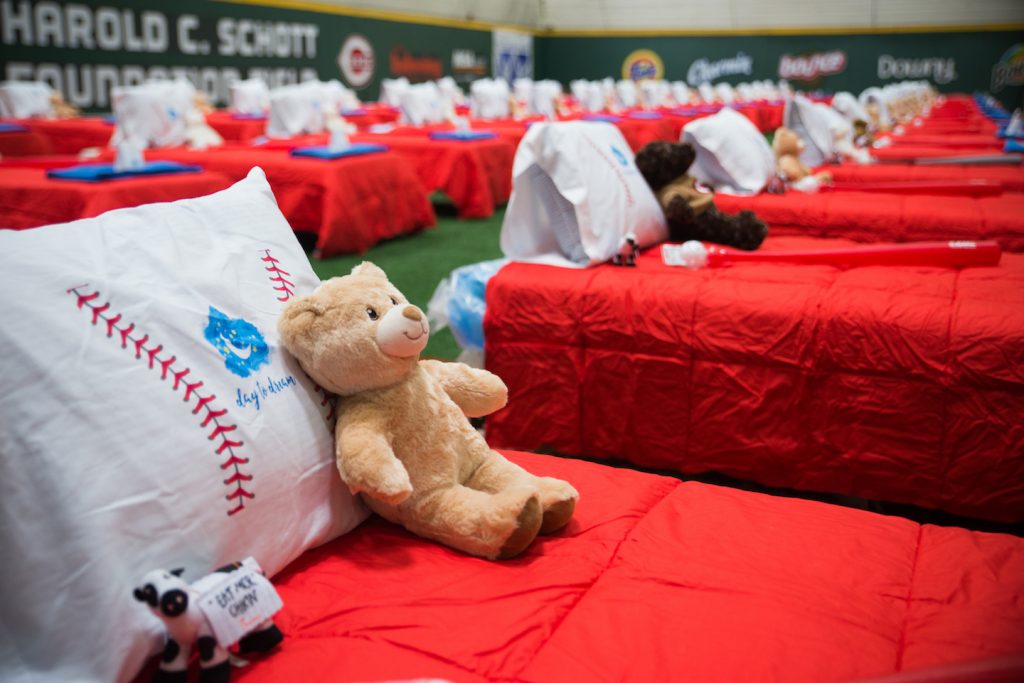 Fifty beds await their new owners. Made up with red comforters and baseball-print pillowcases, each also came with a teddy bear, a stuffed cow, and a bat 