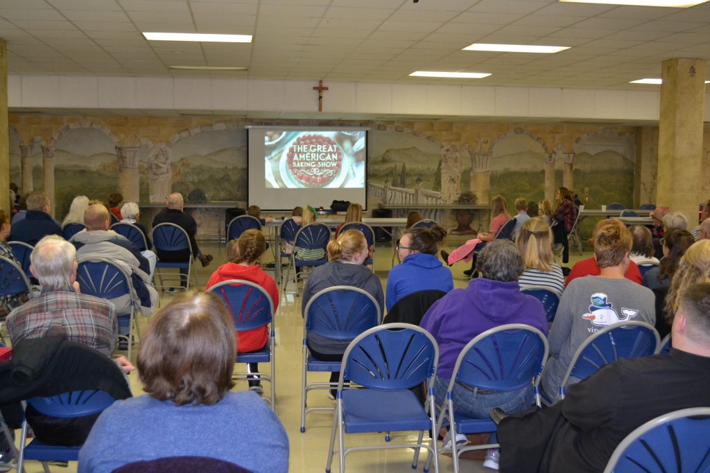 The crowd turned its attention to watching the debut of Father Kyle Schippel in the Great American Baking Show. (CT Photo/Greg Hartman)