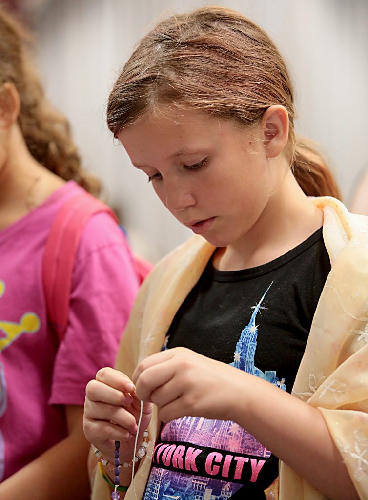 Olivia Klefeker, 10, of the Catholic faith, wears a Muslim hijab on her shoulders as she makes a Rosary during the first Festival of Faiths at the Cintas Center in Cincinnati Sunday, June 24, 2018. (CT Photo/E.L. Hubbard)