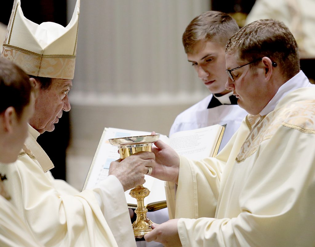 Father Zach Cecil receives the chalice and paten (CT Photo/E L Hubbard)