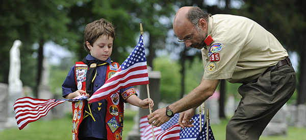 Young Boy Scout and Scoutmaster place U.S. flags at graves of military veterans