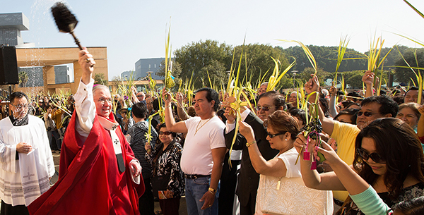 Archbishop Gomez blesses people holding palms with holy water during Palm Sunday Mass outside Los Angeles cathedral