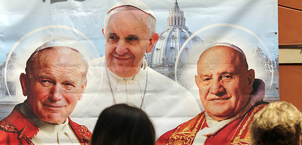 A woman takes a picture of an illustration depicting Blessed John Paul II, left, Pope Francis and Blessed John XXIII outside a shop in Rome April 23. On April 27, Pope Francis canonized both former popes. (CNS photo/Stefano Rellandini, Reuters)