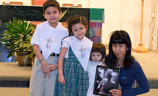 The Evans children, from left, Jimmy, Zoe, and Ashton, pose with their mother, Ao, holding a photo of her deceased husband Richard, after their baptism at St. James of the Valley Church in February. (Courtesy Photo)