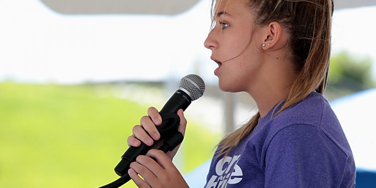 Allison Riegler sings “God Bless America” during the Cross the Bridge for Life celebration on Riverboat Row in Newport, Sunday, June 3, 2018. (CT Photo/E.L. Hubbard)