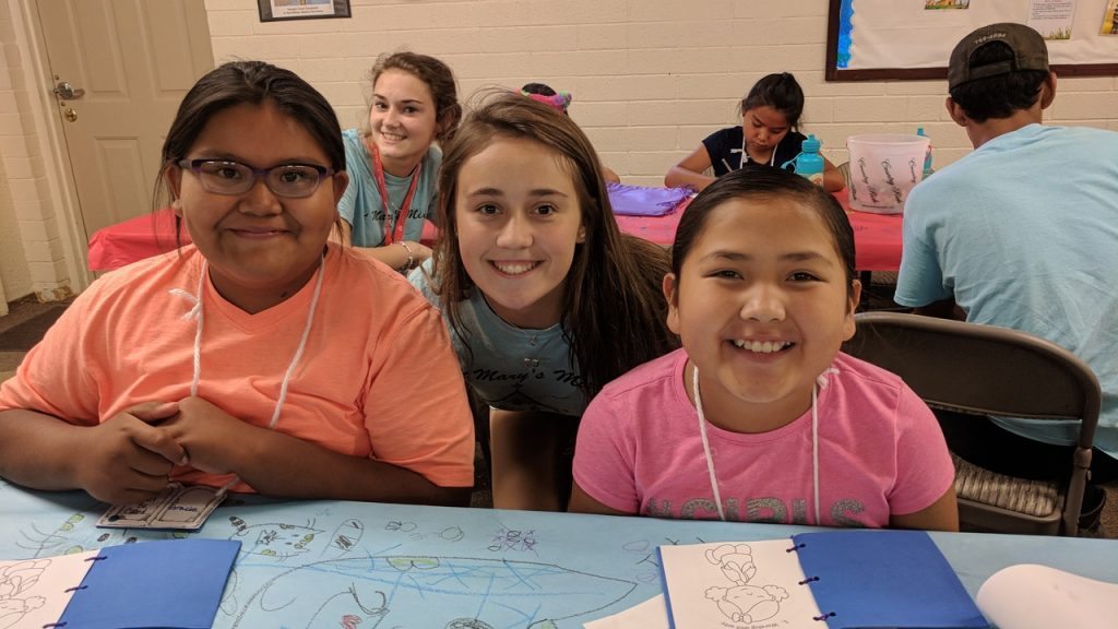 Kylie Schmidt with Savannah Hoover in the background poses with two Navajo children at Summer Bible School. (Courtesy Photo)