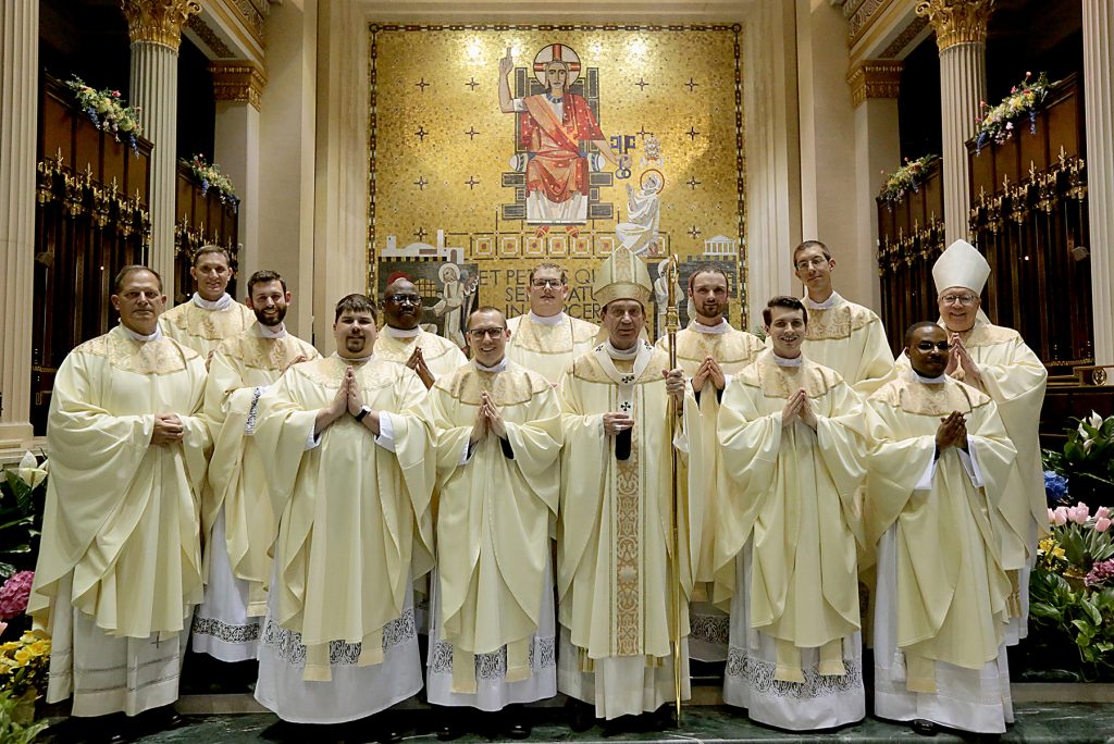 Front Row from L to R: Father Anthony Brausch, Father Mark Bredstege, Father Jeff Stegbauer, Archbishop Dennis M. Schnurr, Father Andrew Hess, Father Alex Biryomumeisho; Back Row L to R, Father Ambrose Dobrozsi, Father Elias Mwesigye, Father Zach Cecil, Father Jedidiah Tritle, Father Christian Cone-Lombarte, and Bishop Joseph Binzer (CT Photo/E L Hubbard)