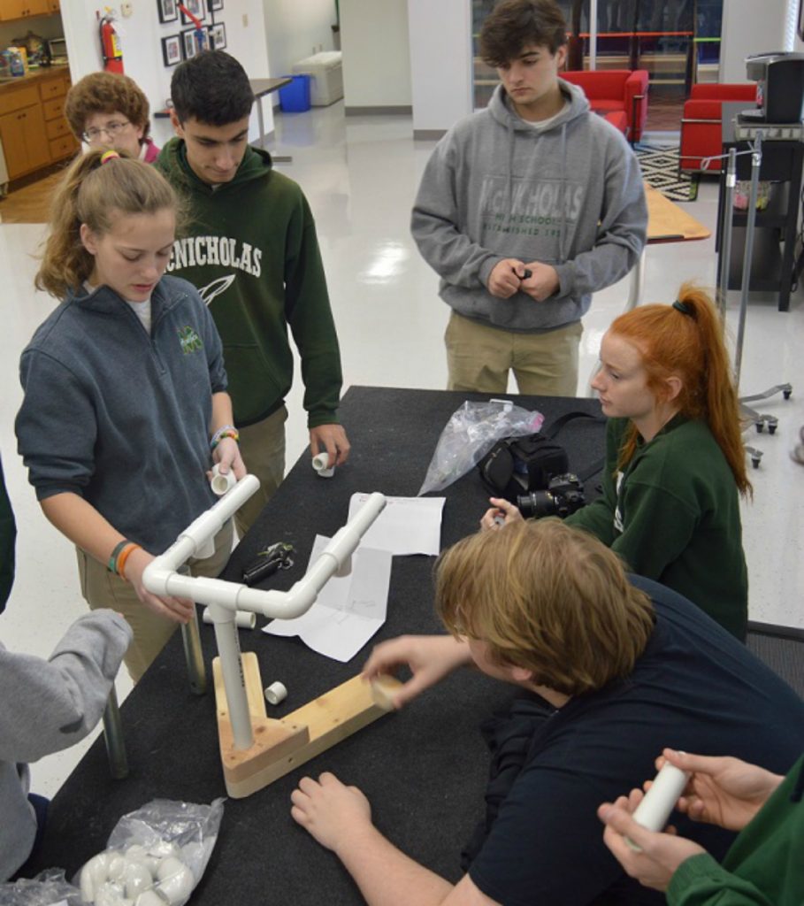 McNicholas High School’s engineering classes have been partnering with alumnus Bill Deimling and his non-profi, May We Help, which designs, creates and builds specialty devices for people with disabilities at no charge. McNicholas engineering students designed a prototype of a machine that students with limited mobility at the Margaret B. Rost School could use to help fill bags.