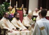 Archbishop Robert G. Casey sits beside two deacons and preaches his homily.